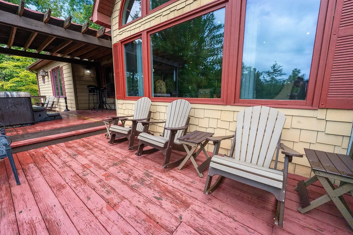 The image features wooden chairs and a hot tub on a spacious deck, with large windows offering views both into and out of the property. The deck is surrounded by trees, creating a seamless blend between the comfort of the accommodation and the wild beauty of the Smoky Mountains.
