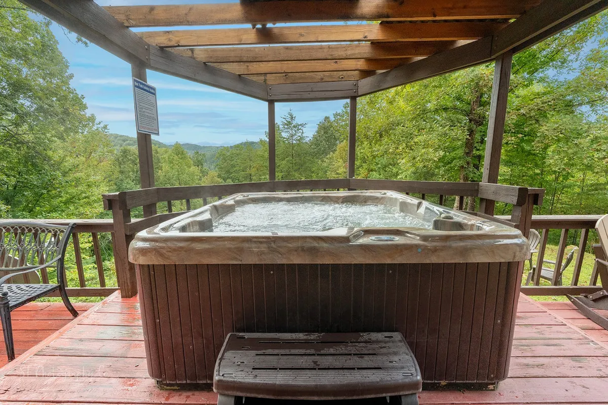An inviting outdoor deck with a hot tub nestled among trees, creating a secluded and peaceful atmosphere. The warm, natural wood of the deck contrasts with the greenery, enhancing the sense of privacy and tranquility.