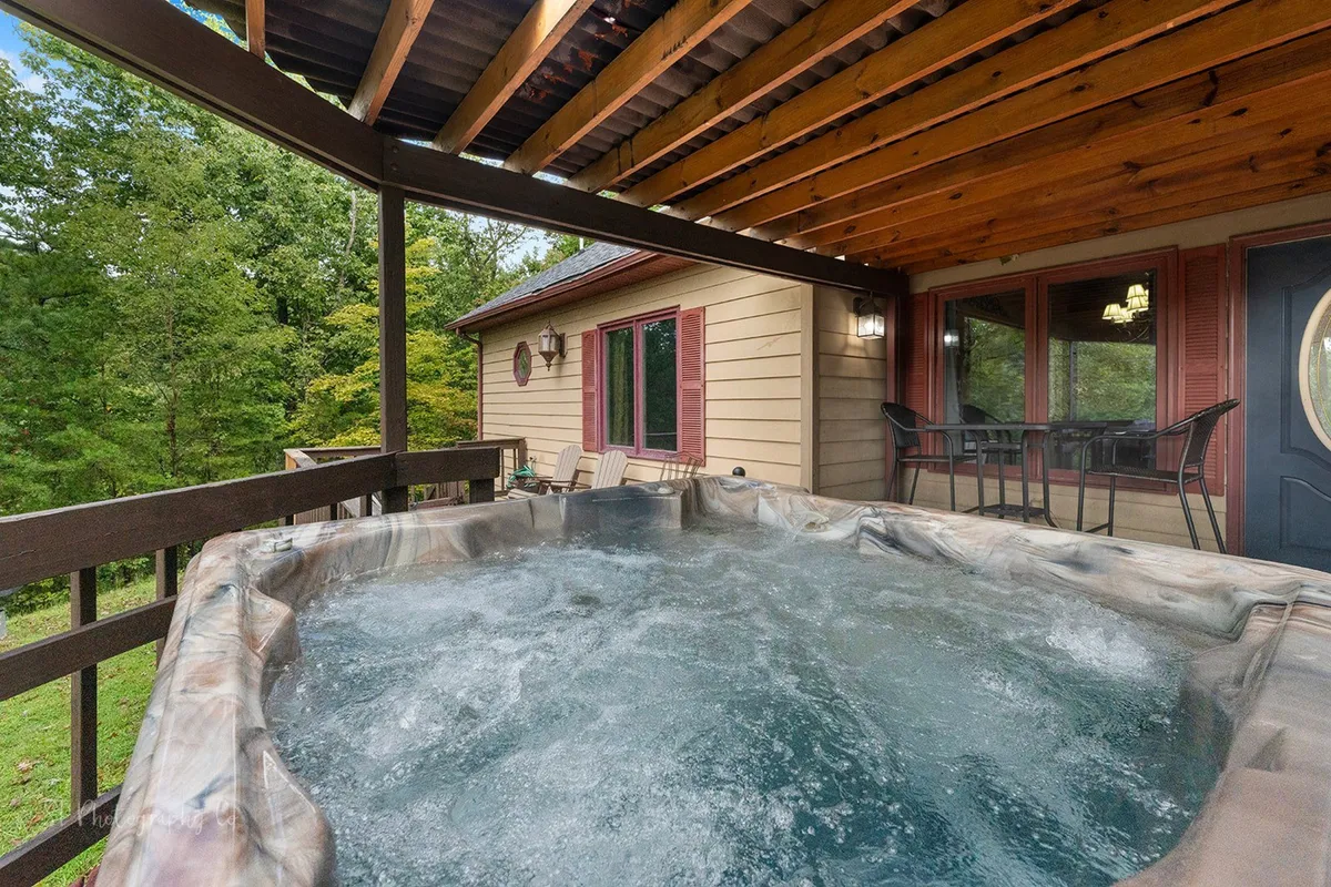 This exterior shot shows the hot tub on a wooden deck adjacent to the house, with the house exterior visible in the background. It captures the welcoming entrance and the inviting outdoor amenities designed for guest enjoyment.