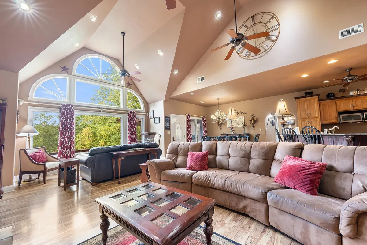 Bright daylight streams through large windows onto a comfortable couch and a stylishly set dining area, accentuating the inviting ambiance of the great room. The space feels perfect for relaxing mornings or lively evening gatherings.