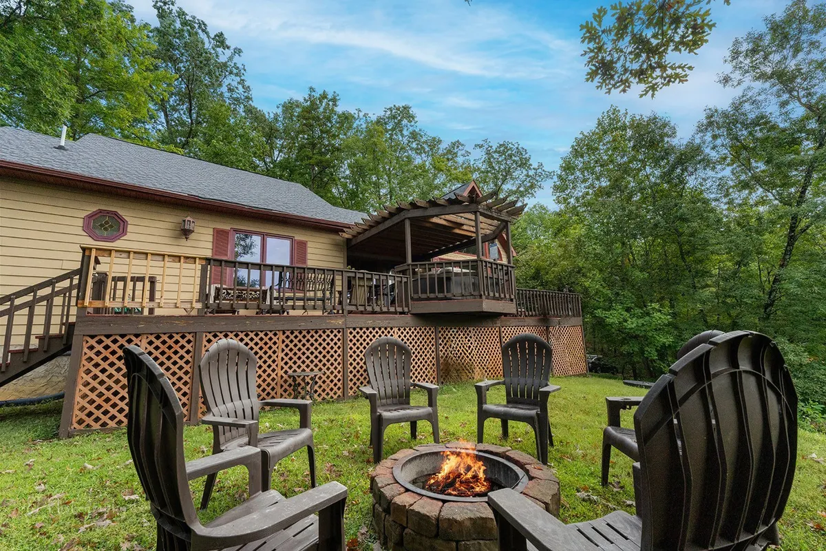 An exterior scene featuring a cozy fire pit area with comfortable seating on a wooden deck, surrounded by trees. The space is primed for campfire gatherings, storytelling, and evening relaxation under the stars.