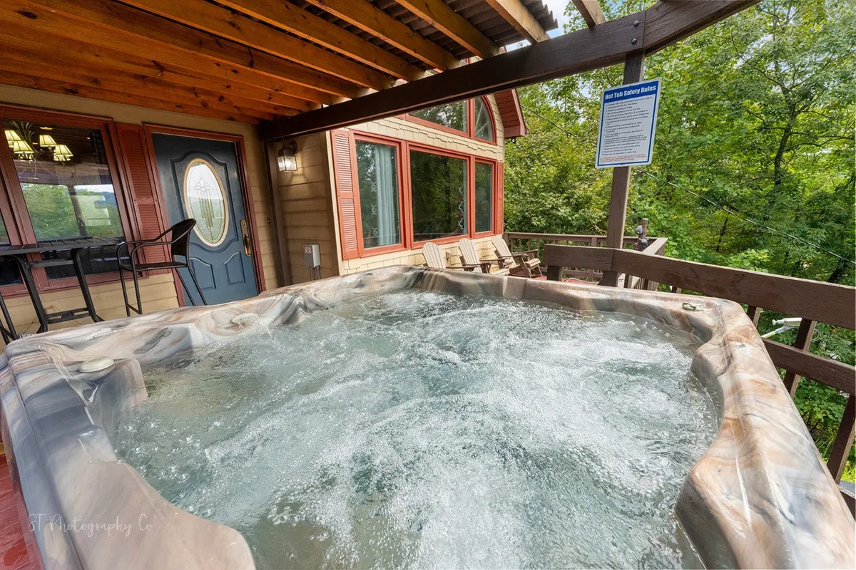 This image shows a tranquil scene of a hot tub set on a wooden deck, surrounded by lush greenery and large windows that reflect the natural light. The space is inviting, with ample room for guests to gather and take in the mountain air. The hot tub is positioned to offer privacy and stunning views, perfect for unwinding after a day of outdoor adventure.