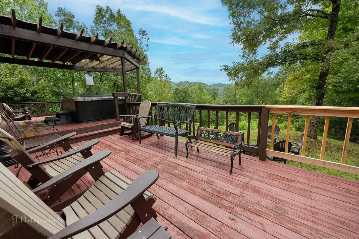 A tranquil outdoor deck featuring a bubbling hot tub surrounded by wooden Adirondack chairs and leafy trees. The scene is set for relaxation, socializing, and soaking after a full day of local attractions or outdoor activities.