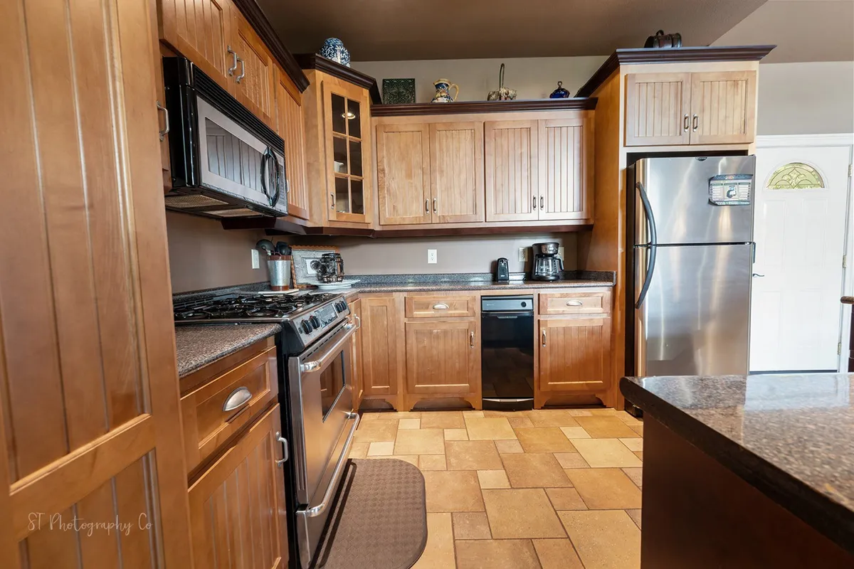 This image highlights a spacious kitchen featuring stainless steel appliances, wooden cabinetry, and granite countertops. The kitchen layout provides ample prep space, and the modern finishes echo the 'chef’s domain' described in the section.