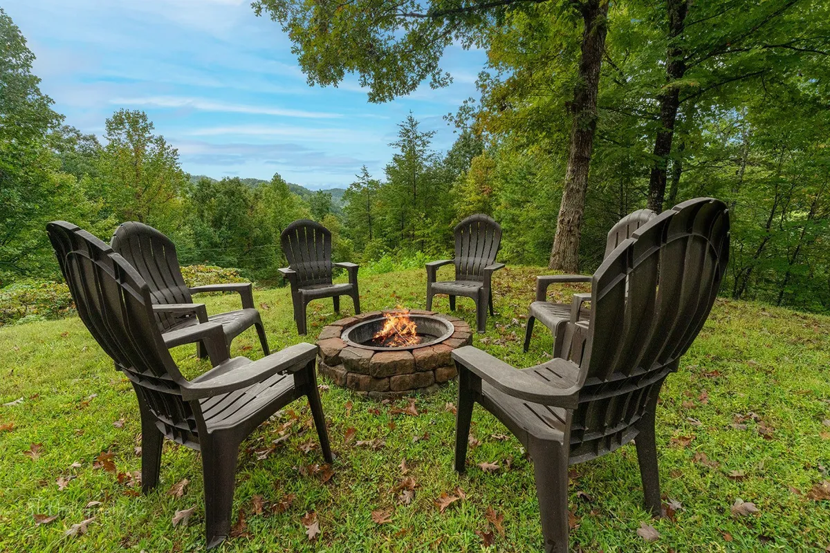 This image shows an inviting fire pit encircled by Adirondack chairs, set amid tall trees. The arrangement suggests a cozy spot for groups to gather, share stories, make s'mores, and enjoy the outdoors, especially in the evening under the stars.