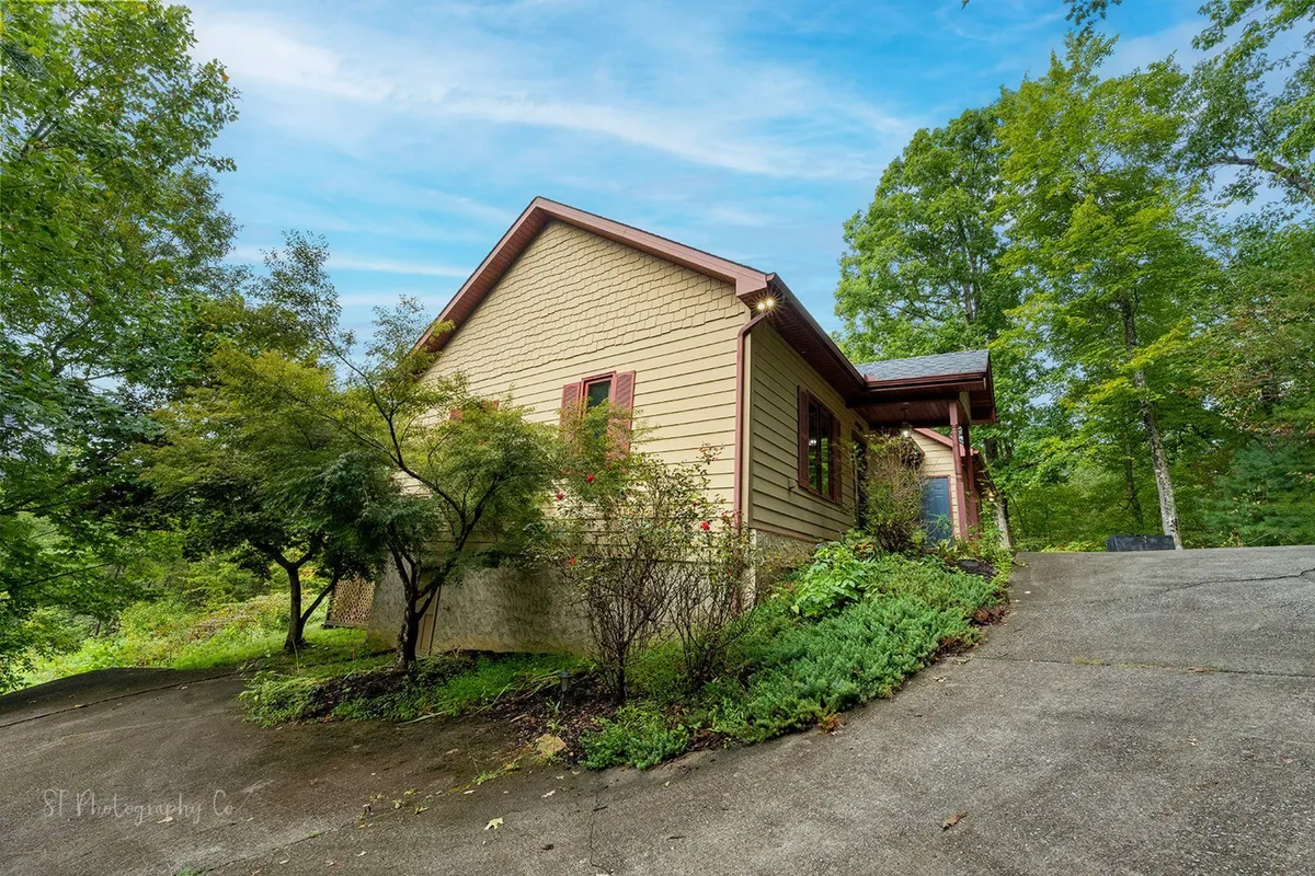 A wide view of the house exterior, driveway, and lush green surroundings. The peaceful landscape and inviting entrance suggest a welcoming atmosphere and opportunities for exploration around the property.